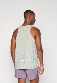 Débardeur en maille gris clair avec une section inférieure texturée et accentuée de motifs dans des teintes de vert ; présente un petit logo rouge à l'arrière.