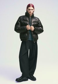 Doudoune noire avec un col haut, surface texturée, fermeture éclair avant et poignets élastiques. Associée à un pantalon noir ample et des chaussures noires chunk.