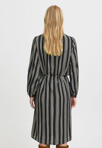 Schwarzes und cremefarbenes gestreiftes Kleid mit langen Ärmeln, tailliertem Schnitt und strukturiertem Stoff; knielang mit geradem Schnitt und leichtem ausgestellten Saum.