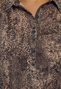 Camicia con stampa leopardata in beige chiaro e marrone, con bottoni anteriori, bottoni neri e un colletto strutturato. Tessuto morbido.
