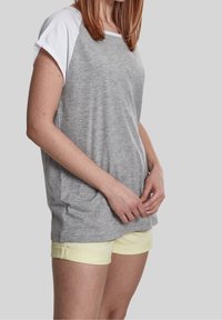 Camiseta raglán gris y blanca de corte holgado, combinada con pantalones cortos amarillos claros. La tela parece suave y casual.