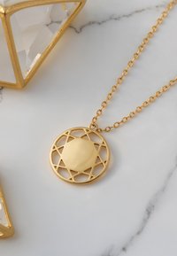Collana con pendente d'oro dal design geometrico circolare e motivo a stella traforata; pietra centrale liscia; posizionata su uno sfondo di marmo.