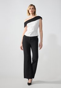 Hvit topp med en off-shoulder svart aksent, tettsittende fasong og teksturerte detaljer. Svart vide bukser fullfører antrekket.
