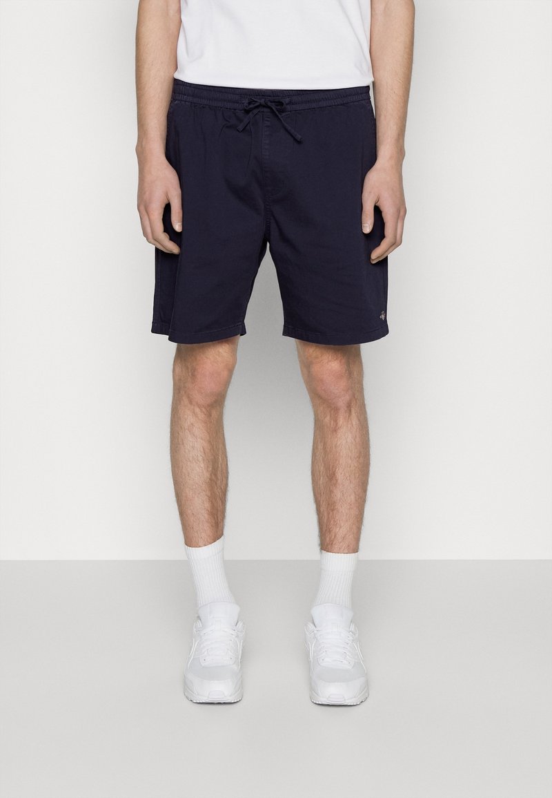 Shorts de bain bleu marine avec une taille élastique, cordon de serrage et poches latérales ; fabriqués en tissu léger et avec une coupe décontractée.