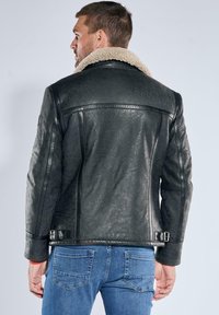 Schwarze Lederjacke mit einem Fellkragen, ausgestattet mit einer glatten Textur, Seitentaschen und Schnallenakzenten an der Taille.