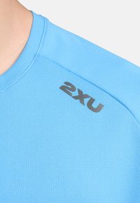 Helevalge sportlik särk tekstureeritud kangaga, millel on must 2XU logo õlal. Lühikesed varrukad ja ümar kaelus.
