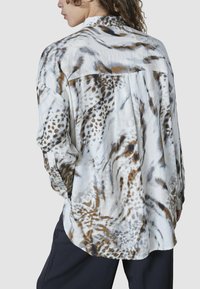 Langærmet skjorte i let, silkeagtigt stof med et mønster af dyreprint i hvid, brun og grå. Løs pasform med bølget kant.