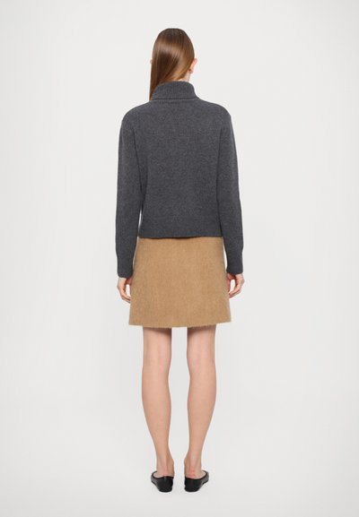 Gray knit sweater with a high collar, paired with a brown textured mini skirt. Model is wearing black slip-on shoes.