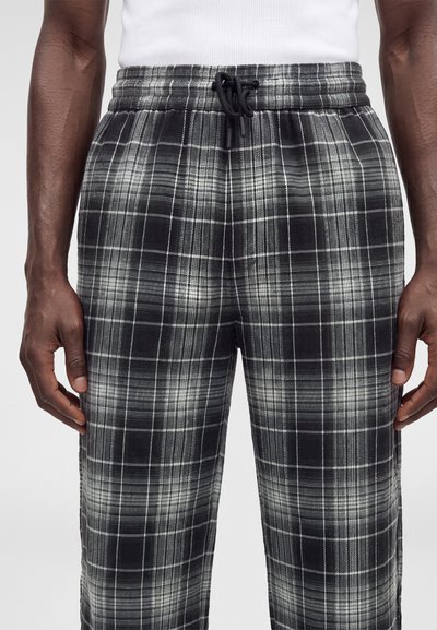 Pantalon à carreaux noir et blanc avec taille élastique et cordon noir, porté par une personne à la peau foncée et un haut blanc.