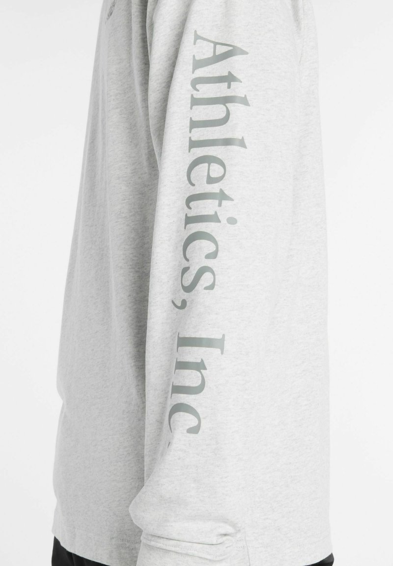 Gray long-sleeve shirt displaying "Athletics, Inc." in a vertical design on the left sleeve. Made from lightweight fabric with a smooth texture.