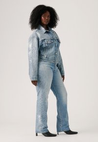 Veste en denim et jean bleu clair avec des motifs de couture décoratifs en argent. Des bottes noires à talons hauts complètent la tenue.
