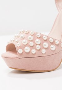 Sandale à plateforme en daim rose avec bout ouvert et diverses tailles d'ornements en perles blanches sur la bride avant.