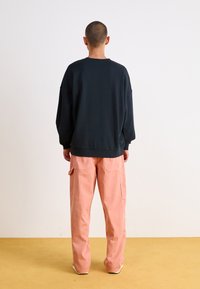 Svart oversized sweatshirt med sjunkna axlar, kombinerad med lösa rosa cargo-byxor med sidfickor, sedd bakifrån.