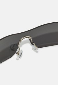 Gafas de sol con lentes oscuros, un diseño negro elegante, puente de metal con acentos plateados y almohadillas nasales transparentes para mayor comodidad.