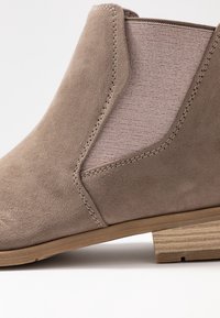 Taupe suede ankle boot featuring elastic side panels, stitched detailing, and a low stacked wooden heel. Smooth texture with a sleek design.