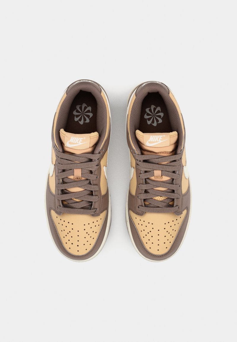 Baskets Nike avec un schéma de couleurs beige et marron, présentant des perforations, des matériaux texturés, ainsi qu'un design de languette et de col rembourrés.
