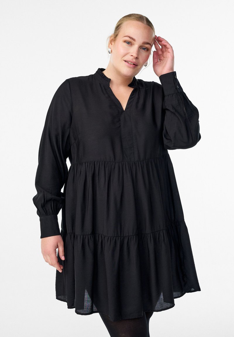 Must mustriga mustikas, pikkade varrukatega, V-kaelusega ja kogutud detailidega. Valmistatud pehmest kangast, voogava kujuga ja põlvekohale ulatuva servaga.