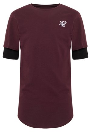 Mørkerød kortærmet skjorte lagd over en sort langærmet skjorte, med hvide stiliserede initialer logo på venstre bryst.