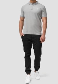 Polo gris à manches courtes, avec patte de boutonnage à trois boutons et logo sur la poitrine gauche, associé à un pantalon noir fuselé et des baskets blanches.