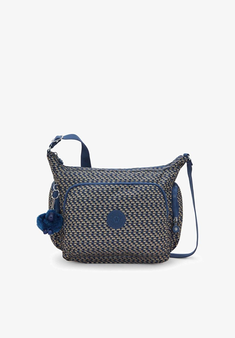 Sac d'épaule en tissu tissé bleu et beige avec une poche avant zippée, un écusson rond avec logo, et un pendentif bleu pelucheux attaché.