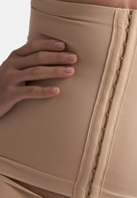Indumento beige a vita alta realizzato in materiale testurizzato e elastico. Presenta una cucitura centrale con cuciture decorative a spirale lungo il lato.