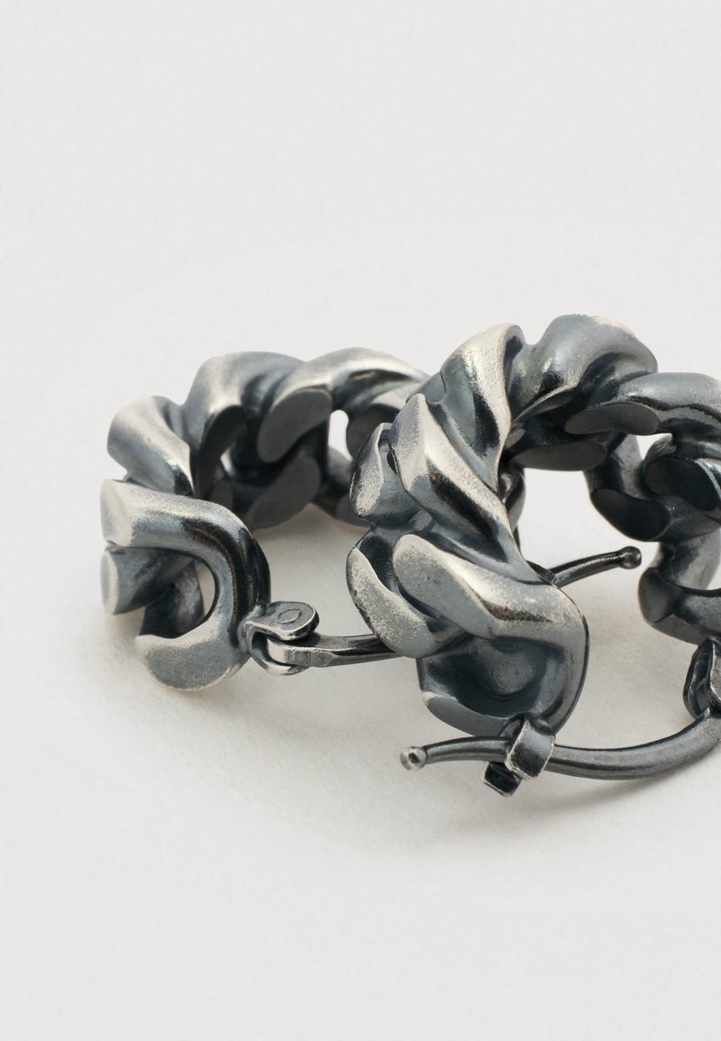 Boucles d'oreilles en métal en forme d'anneau avec un design torsadé et une finition gris métallique, présentant des textures lisses et une brillance subtile.