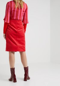 Rode corduroy rok met verticale ribbels, gecombineerd met een rode top met roze strepen en uitlopende mouwen. Glanzende bordeauxrode enkellaarzen.