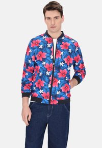 Blauwe bloemen bomberjack met grote rode bloemen en witte accenten. Zwarte geribde boorden en zoom, met een ritssluiting aan de voorkant.