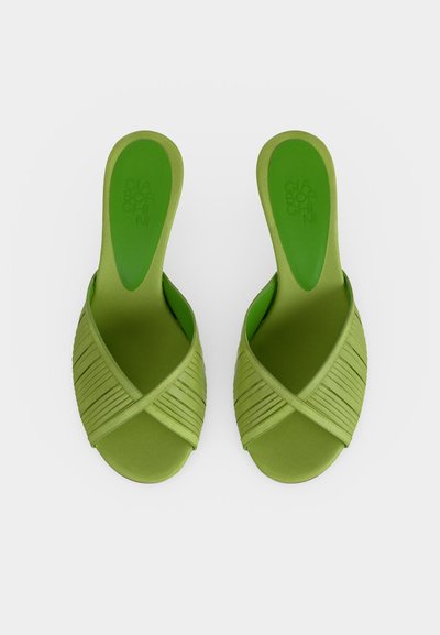 Πράσινα σανδάλια τύπου slip-on με λουριά που διασταυρώνονται και επίπεδες σόλες, φαινόμενα από πάνω σε λευκό φόντο.