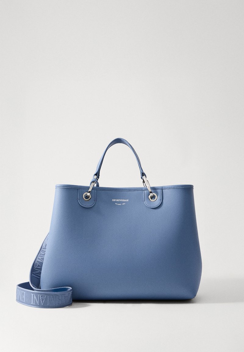 Τσαντάκι tote από μαλακό υλικό σε ανοιχτό μπλε χρώμα με ανάγλυφη υφή, με ασημί μεταλλικά στοιχεία, διπλές λαβές και αποσπώμενο λουράκι που διαθέτει την λεπτομέρεια του λογότυπου της μάρκας.