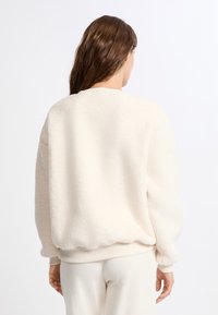 Felpa in pile color crema con un esterno morbido e testurizzato. Presenta un collo rotondo, polsini a coste e una vestibilità comoda.