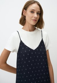 Marineblauwe slipdress met bloempatronen en fijne strepen, gedragen over een witte T-shirt. Verstelbare dunne banden en een V-hals ontwerp.