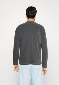 Sudadera de manga larga en color gris oscuro, fabricada con tejido suave, con un cuello redondo y mangas con puños. Diseño liso, sin patrones visibles.