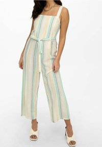 Combinaison rayée aux couleurs pastel avec un décolleté carré, jambes larges, et une ceinture en tissu à la taille. Fabriquée en matériau léger et texturé.