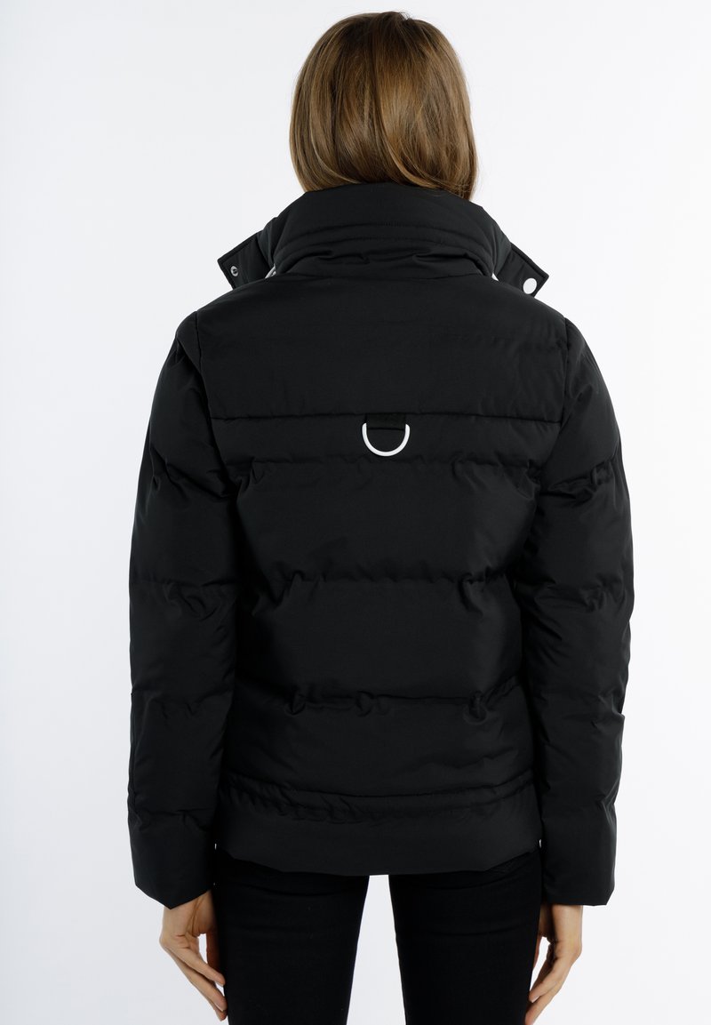 Doudoune noire avec un col haut, des accents de boutons et un détail en D-ring au dos. Texture épaisse et matelassée pour la chaleur.