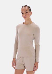 Beige pitkähiha-paita ja siihen sopivat shortsit, valmistettu sileästä kankaasta. Mallissa pyöreä pääntie ja shortsien vähäeleinen logo.