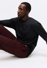 Schwarzes Langarmshirt mit emblemiertem "HUGO"-Logo. Rote und schwarze gemusterte Hose mit geometrischen Formen und einem gebrandeten Bund.