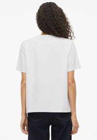 Hvid T-shirt med korte ærmer, afslappet pasform og rund halsudskæring, lavet af blødt bomuldsmateriale. Bagtilladen viser minimal detaljering.