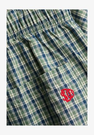 Groen, blauw en wit geruit stof met elastische tailleband en een klein rood geborduurd logo op een zak.