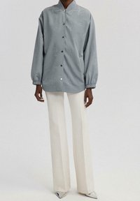 Lyseblå jakke med ståkrave, trykknapper og et diskret mønster over det hele. Parret med cremefarvede brede bukser og sølvfarvede spidse sko.