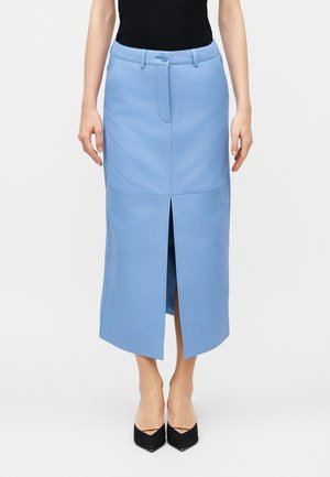 Γυναίκα που φοράει μια φούστα μέσης ψηλής, μήκους μέχρι τη μέση της γάμπας, ανοιχτού μπλε χρώματος, με κεντρικό άνοιγμα μπροστά, κουμπί και θηλιές για ζώνη, σε συνδυασμό με μαύρες μυτερές γόβες.