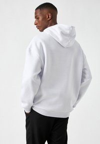 Sudadera gris claro hecha de una mezcla de algodón, con un bolsillo tipo canguro y puños de canalé. Textura suave con un ajuste holgado y capucha centrada.