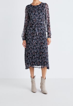 Langärmliges, navy Blaues Kleid mit floralem Muster, Taillengürtel und gestuften Texturen. Getragen mit hellgrauen Cowboy-Stiefeln.