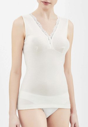Donna che indossa un top bianco senza maniche con rifiniture in pizzo intorno allo scollo a V e biancheria intima bianca abbinata su uno sfondo semplice.