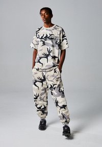 Grijze t-shirt met camouflagepatroon en bijpassende broek in een comfortabele fit, met een logo op de borst en elastische boorden bij de enkels.