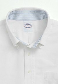 Bílá košile s knoflíky a kontrastním světle modrým proužkovaným vnitřním límcem a kapsou, vyrobená z tkané bavlněné látky. Viditelná značka.