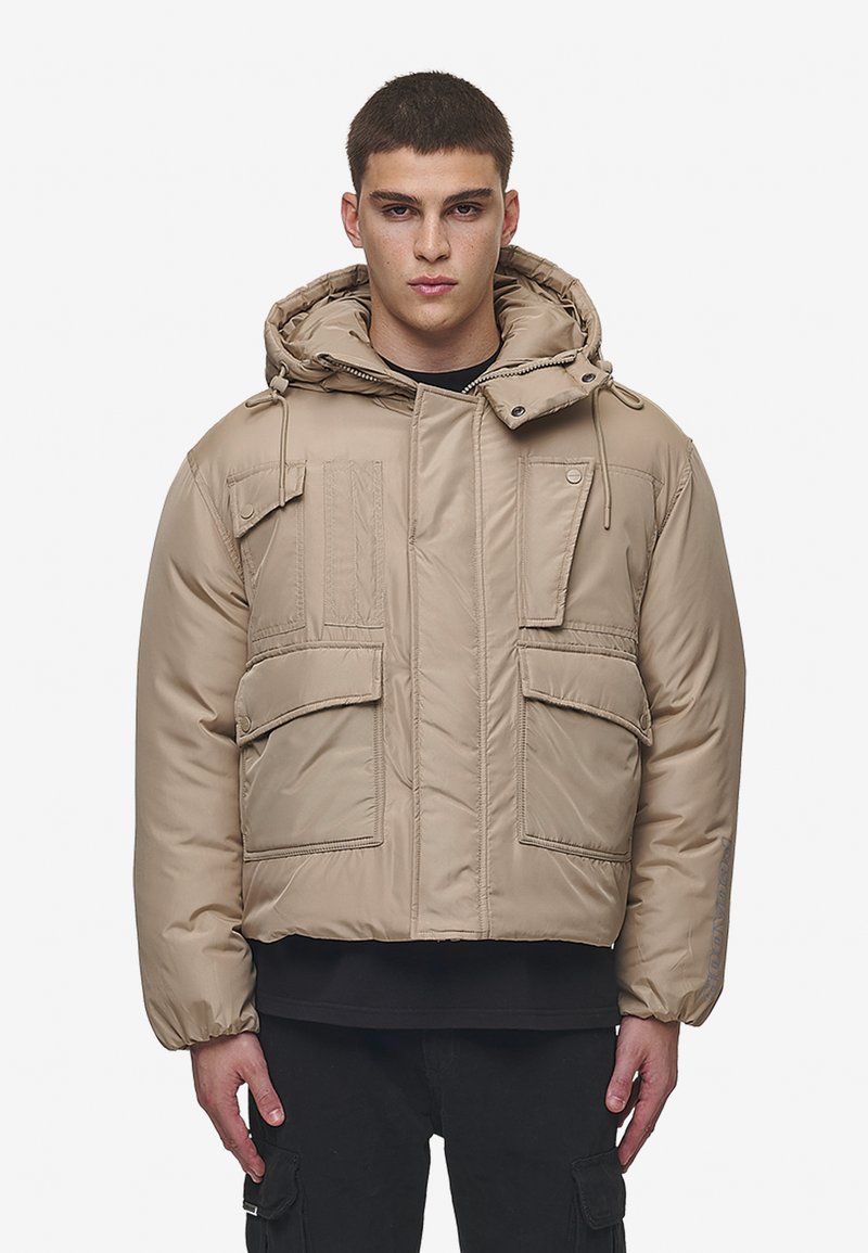 Beige pufferjakke med hette, som har flere frontlommer, glidelås og elastiske mansjetter. Glatt, polstret stoffstruktur.