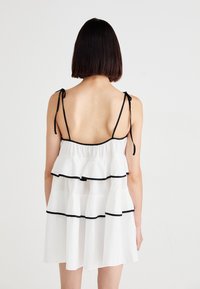 Robe blanche à volants avec ourlet noir, dotée de bretelles spaghetti et d'une coupe décontractée. Le dos présente un design ouvert avec des fermetures à nouer.
