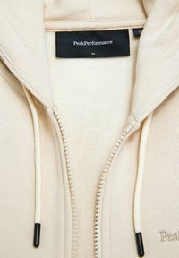 Lynlås hættetrøje i lys beige, lavet af blødt stof med fleecefor, og har off-white snore og logo broderi.
