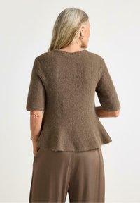 Top in maglia marrone a maniche corte con finitura testurizzata, orlo peplum, scollatura rotonda e bordi leggermente sfilacciati, abbinato a pantaloni marroni lisci.